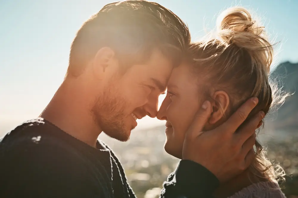 A happy couple embracing closely with their foreheads touching, smiling at each other under the sunlight, symbolizing intimacy, connection, and sexual wellness.