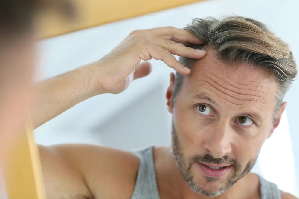 A middle-aged man examining his hairline in the mirror, checking for signs of hair thinning or hair restoration progress.